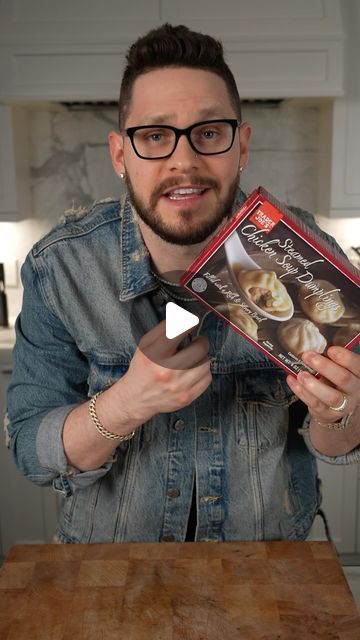 a man holding up a box of food in his hand while standing next to a wooden table