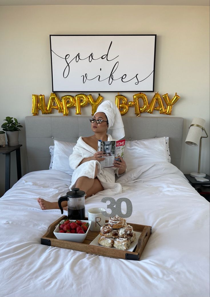 a woman is sitting on her bed reading a book and having breakfast with some coffee