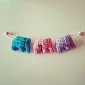 three crocheted elephants hanging on a clothesline with two pink, one blue and one green