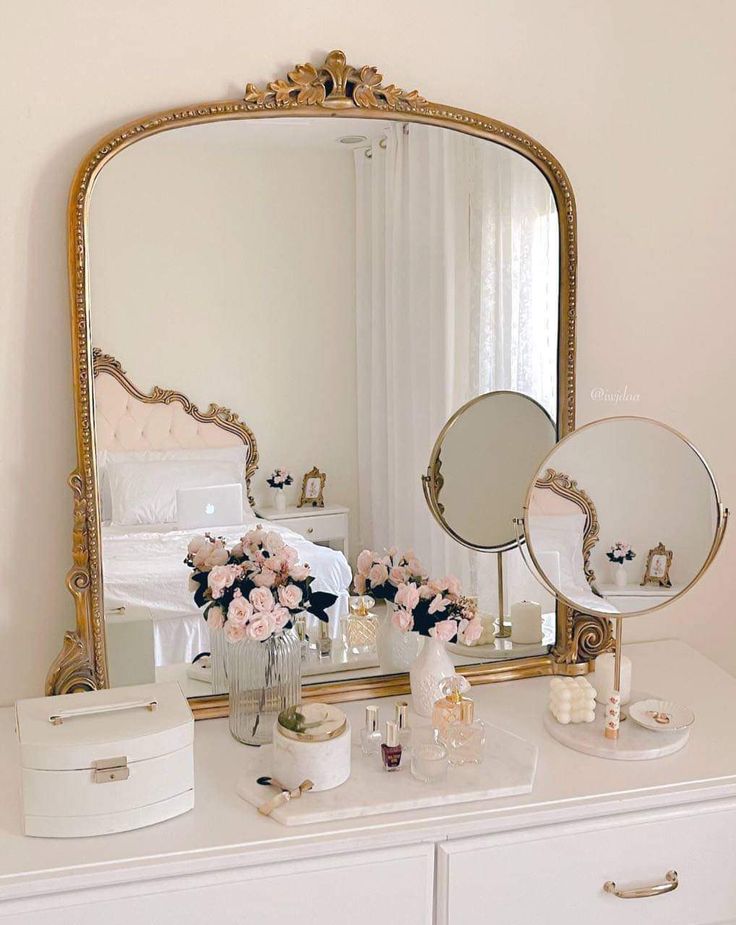 a white dresser topped with a mirror and vase filled with pink flowers on top of it