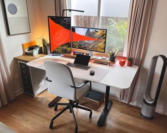 a desk with a laptop and two monitors on it, in front of a window