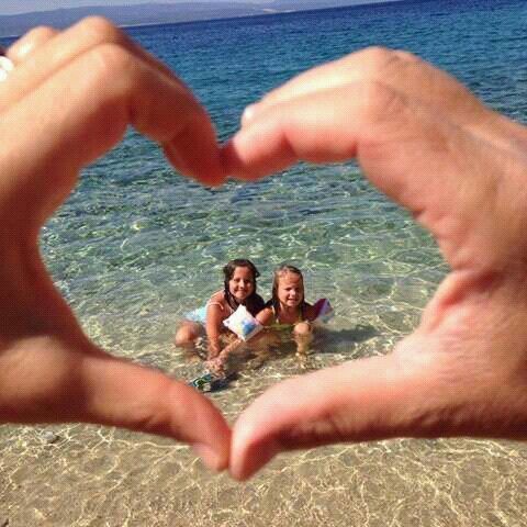 two people making a heart shape with their hands in the water on a sunny day