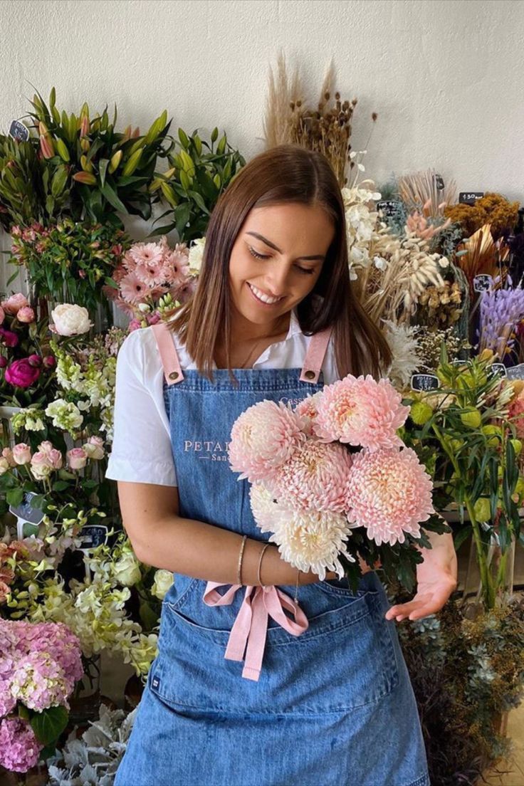 a woman in overalls holding flowers and smiling