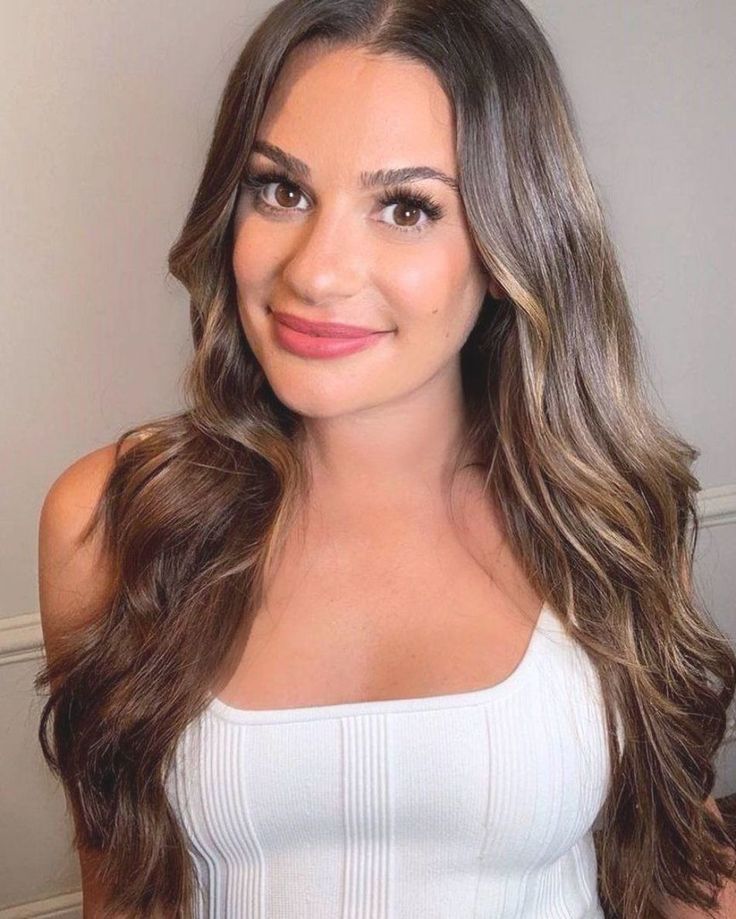 a woman with long brown hair wearing a white top and looking at the camera while smiling