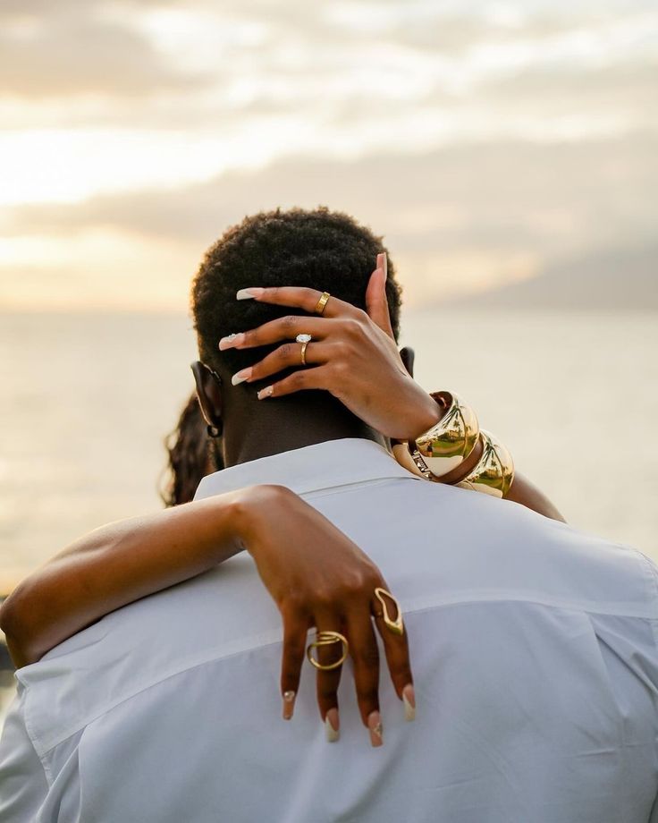 a man and woman embracing each other in front of the ocean with rings on their fingers