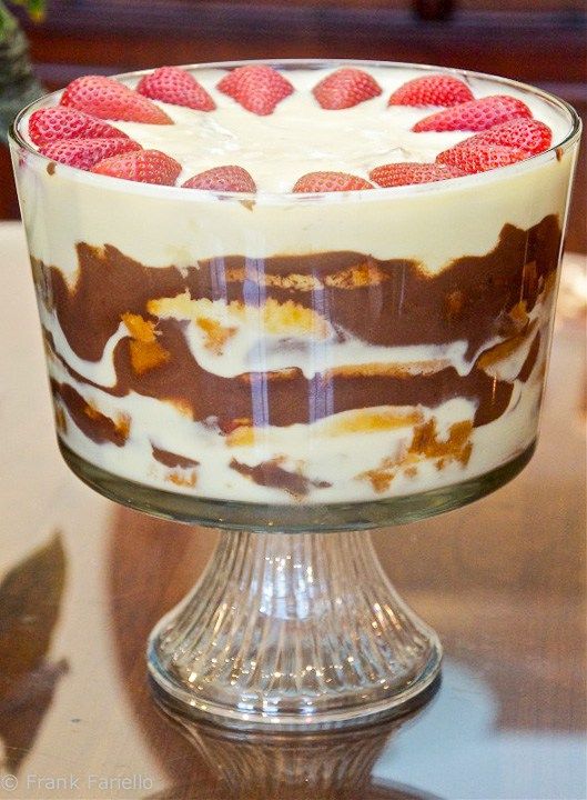 a trifle with strawberries on top is sitting on a glass pedestal, ready to be eaten