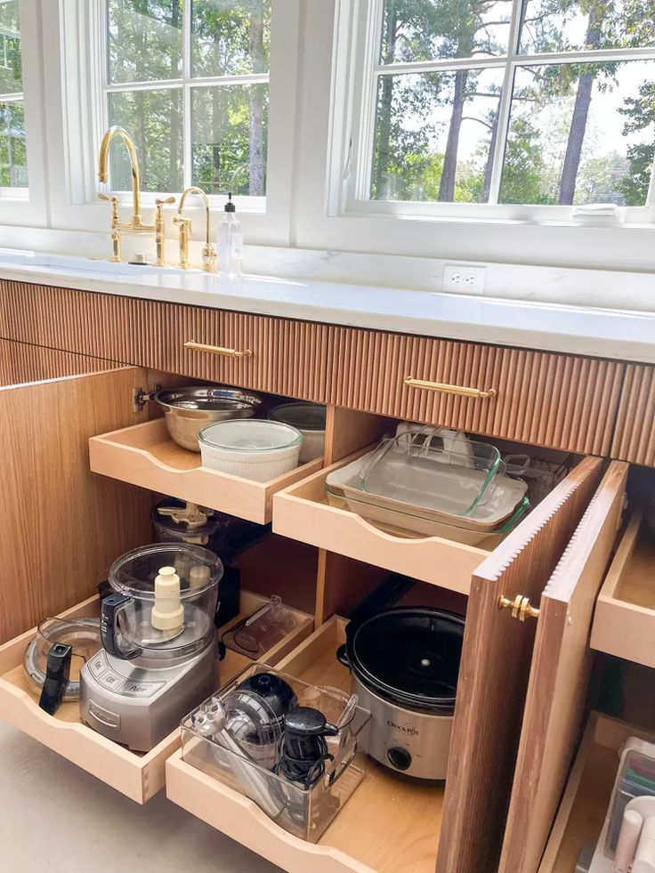 an open drawer in a kitchen with pots and pans on the bottom shelf, next to a window