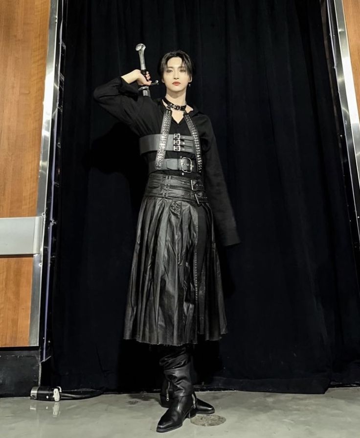 a woman standing in front of a black curtain holding a hammer up to her head