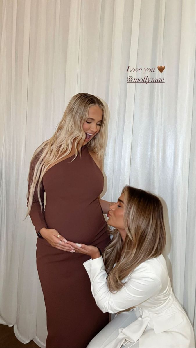 two women in white dresses standing next to each other and one is touching her pregnant belly