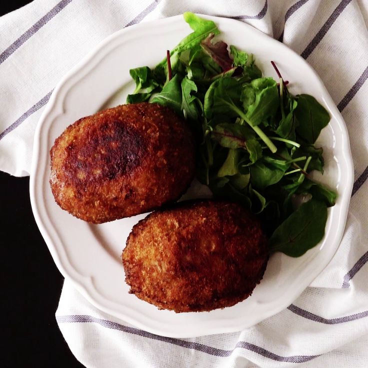 two fried meat patties on a white plate next to a green leafy salad