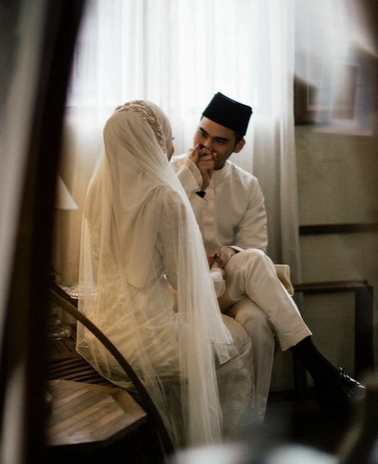 a man and woman sitting next to each other in front of a window with sheer curtains