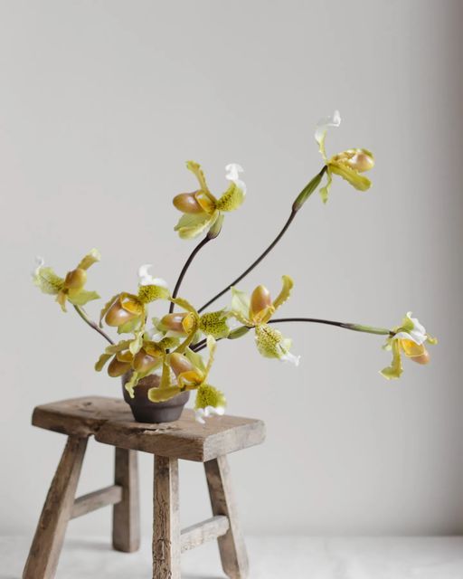 a small wooden stool holding a potted plant on it's side, with yellow and white flowers in the center