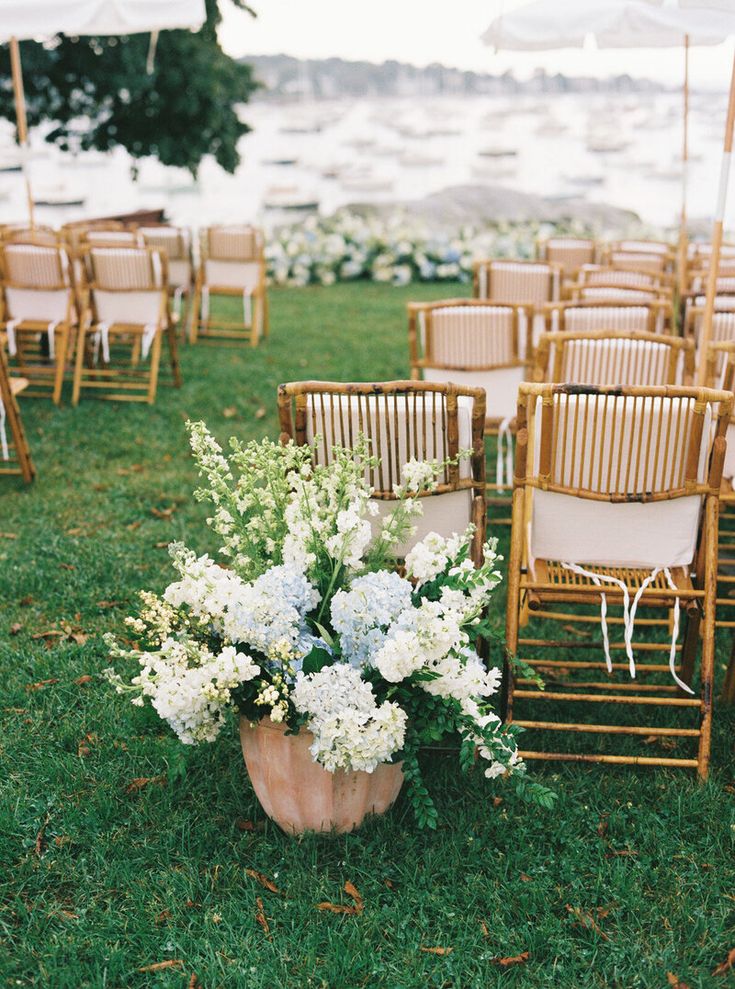 an outdoor ceremony setup with chairs, flowers and umbrellas on the grass by the water