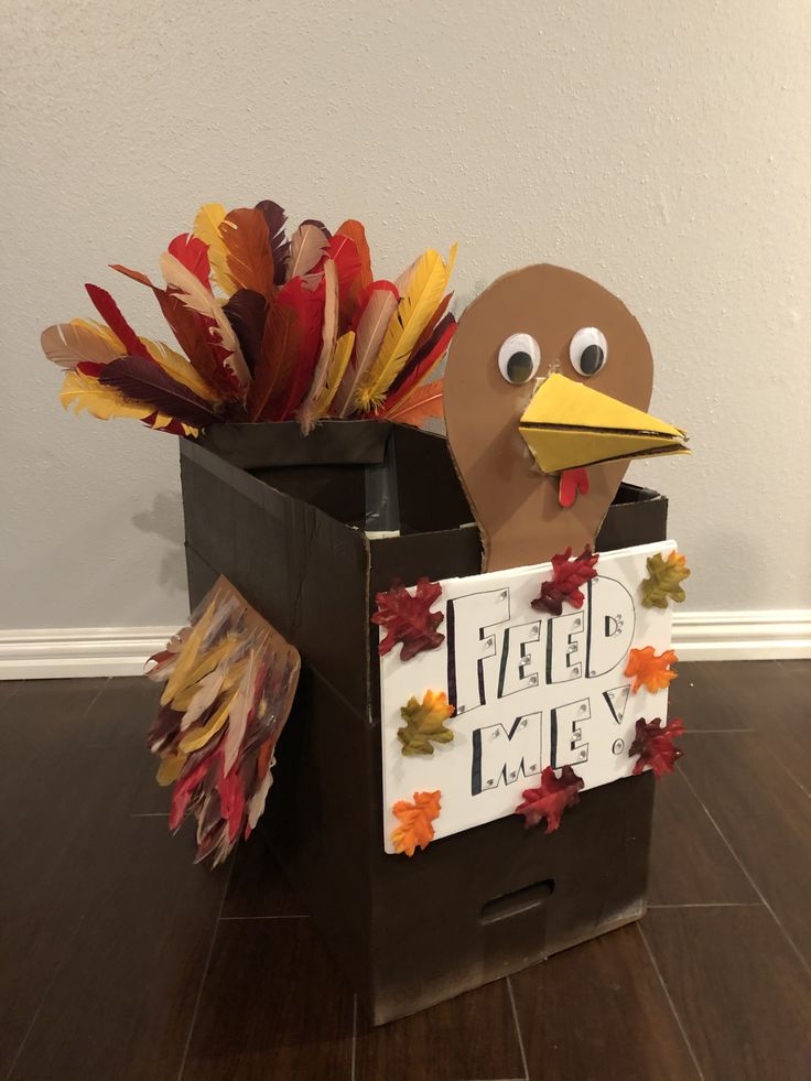 a cardboard turkey sitting on top of a box with leaves in it's mouth