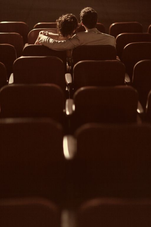 two people sitting in an empty auditorium with their arms around each other's shoulders