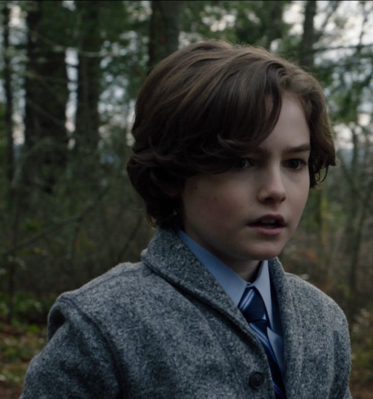 a young boy wearing a coat and tie in the woods