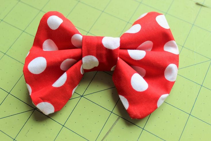 a red and white polka dot bow on a green cutting mat with scissors next to it