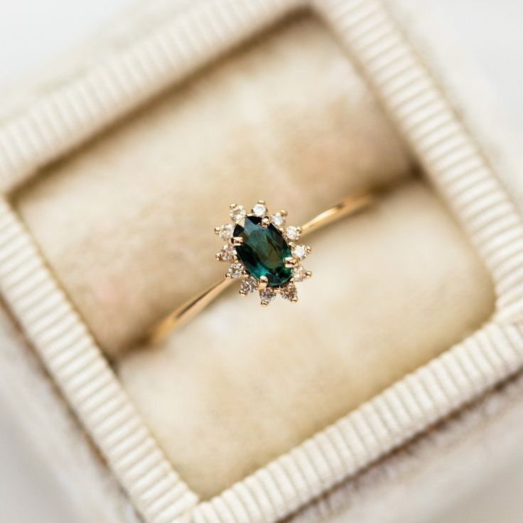 an engagement ring with a green stone surrounded by small white diamonds in a velvet box