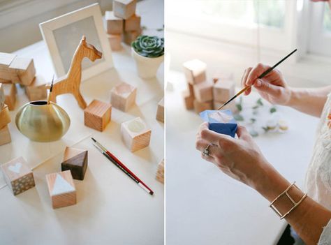 a woman holding a paintbrush in her right hand and painting wooden blocks on the left