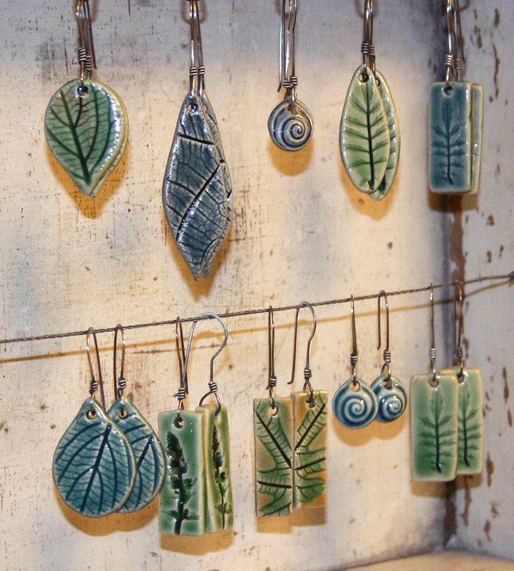 a bunch of leaf shaped earrings hanging from hooks on a wall next to each other