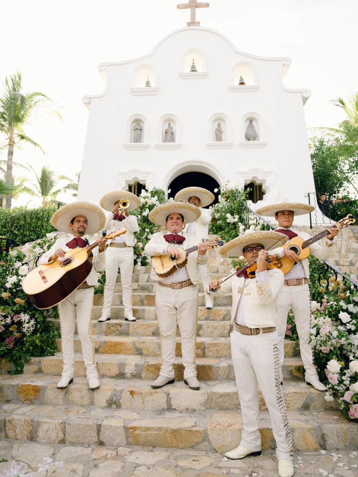 three men in white outfits are playing guitars and singing on the steps to a church