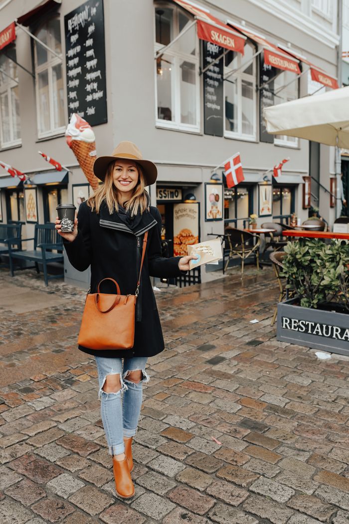 a woman wearing a hat and holding an ice cream cone in her hand while walking down the street