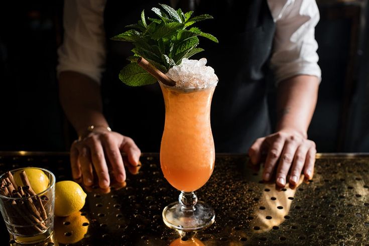 a person holding a drink on top of a table next to lemons and ice