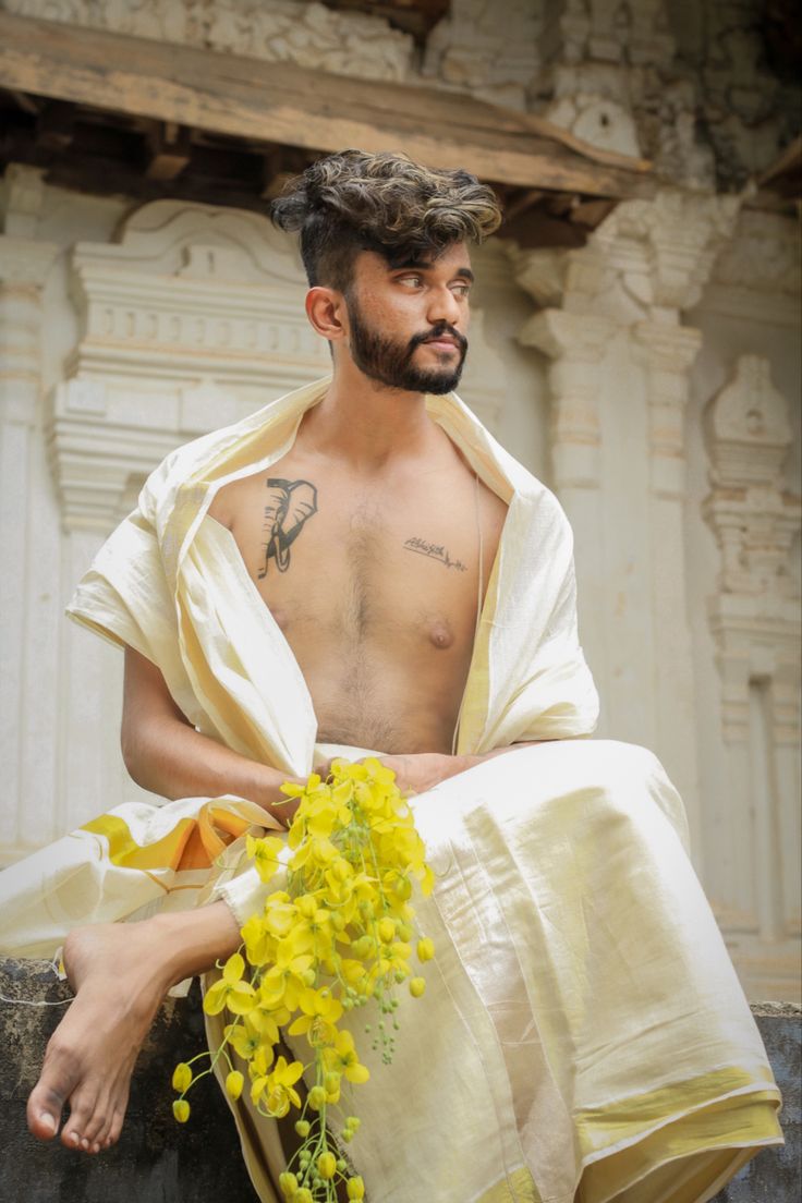 a man sitting on top of a stone wall next to yellow flowers in front of him