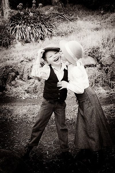 two children are playing with each other in black and white photo, one is wearing a hat