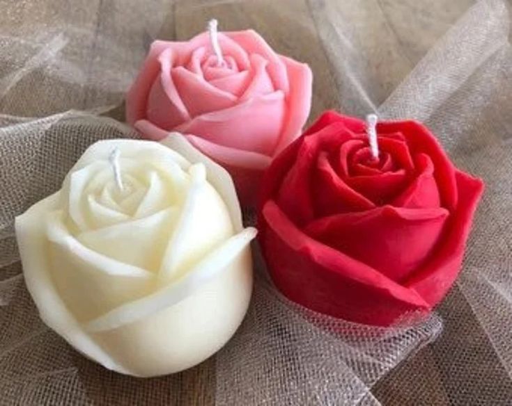 three different colored roses sitting on top of a cloth covered tablecloth with one candle in the middle