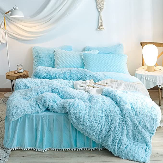 a bed with blue comforters and pillows in a room next to a lamp on a table