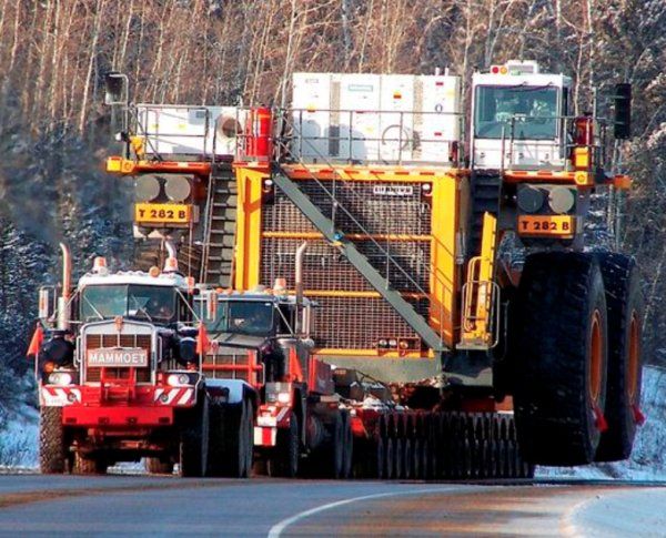 two large trucks driving down the road with trees in the backgrouund and snow on the ground