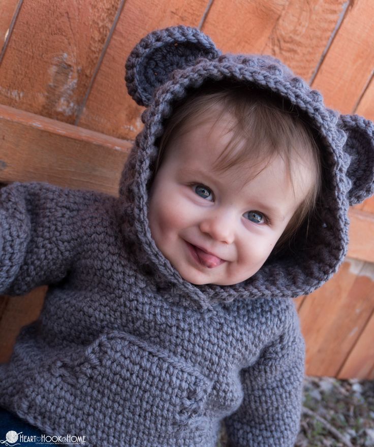 a small child wearing a gray knitted bear hoodie and smiling at the camera