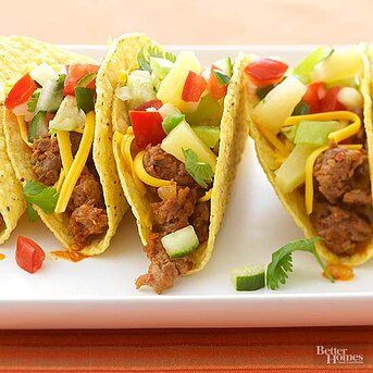 three tacos with meat, pineapple salsa and peppers on a white platter