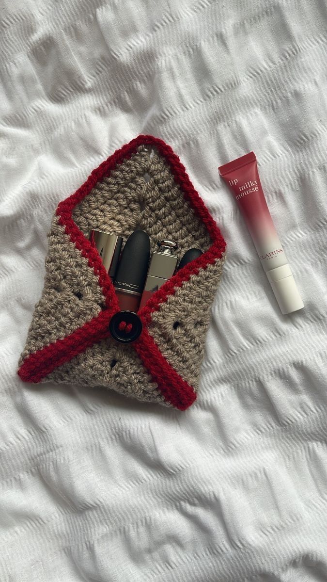 a crocheted bag with cosmetics and lipstick on it sitting on top of a bed