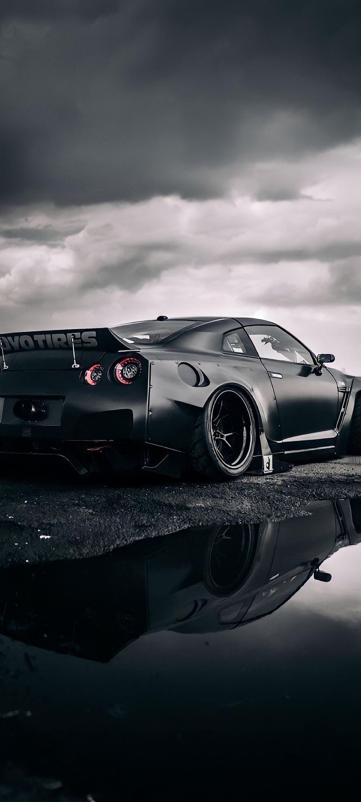 a black sports car parked on the side of a road with dark clouds in the background