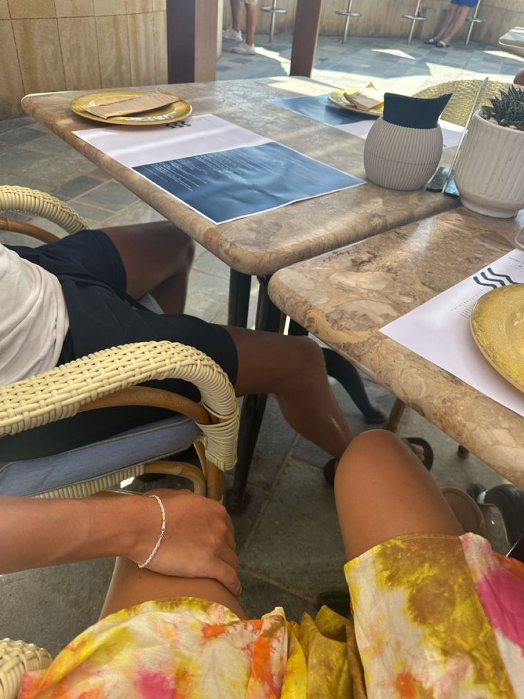 two people sitting at a table with plates and bowls on it, one person has their feet up against the table