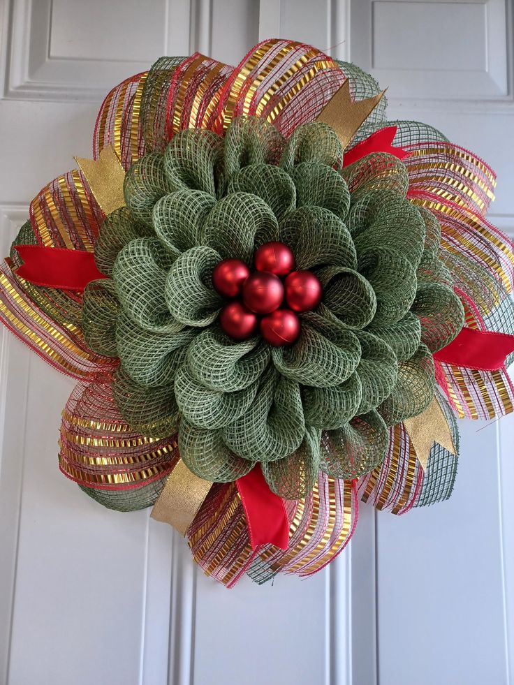 a green wreath with red balls and ribbon hanging on the front door ornament