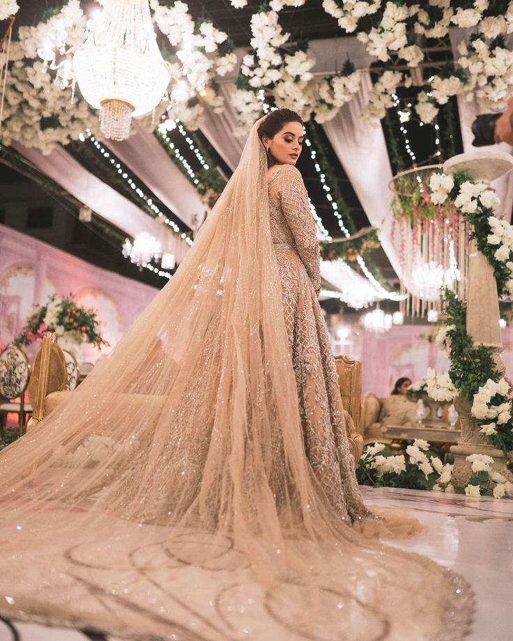 a woman in a wedding dress standing under a chandelier with flowers on it