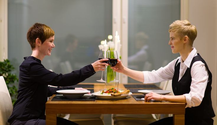 two people sitting at a table with plates and glasses of wine in their hands,