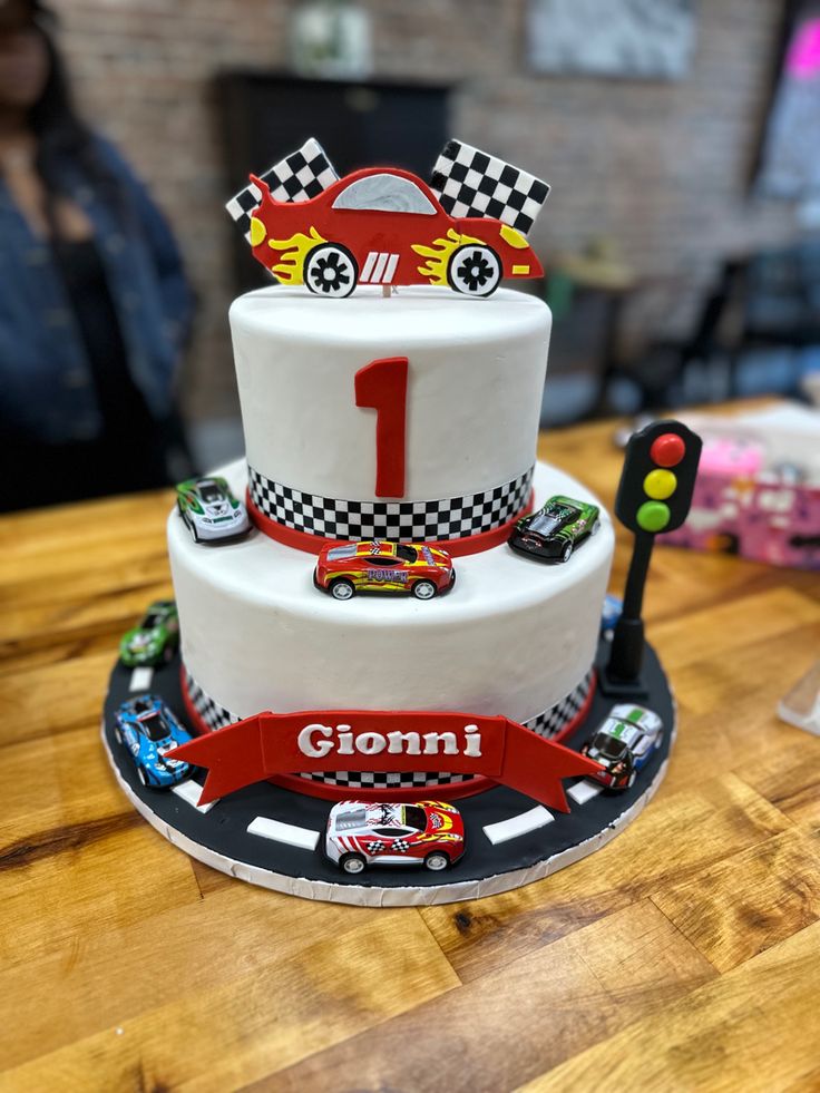 a three tiered cake with cars on the top and number one on the bottom