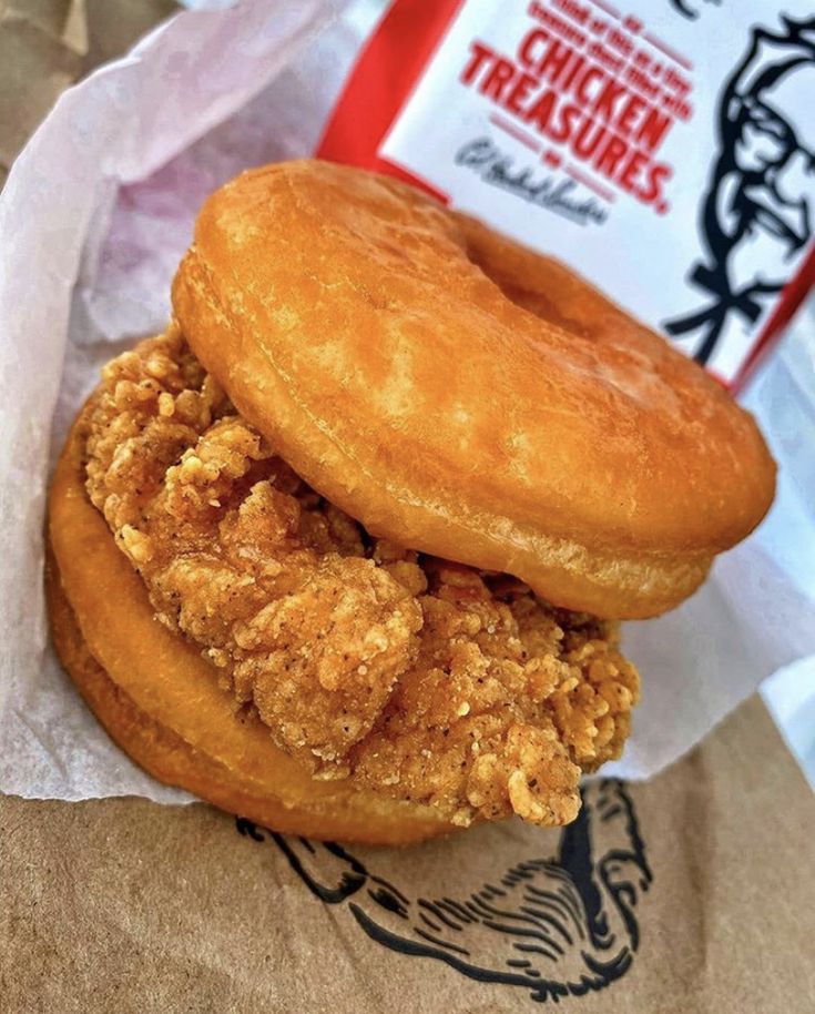 a fried chicken sandwich in a paper bag next to a packet of chicken treasuress