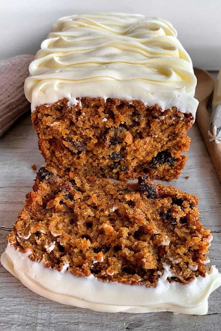 carrot cake with white frosting and raisins cut in half on a wooden table