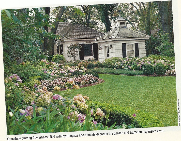 an old house surrounded by lush green grass and flowers in the foreground is a garden with pink and white hydrangeas