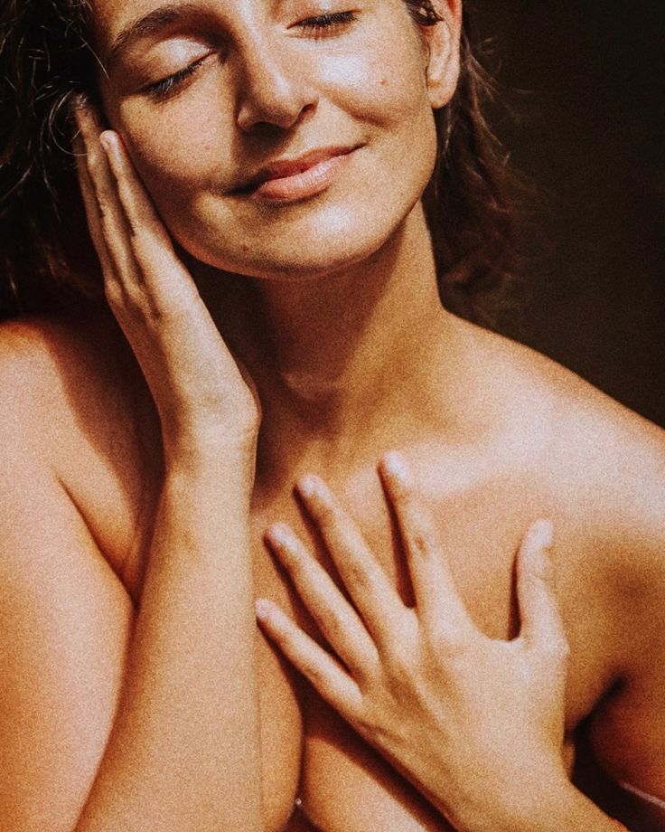 a naked woman with her hands on her chest looking at the camera while she smiles