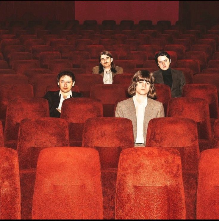 three men sitting in rows of red chairs with their backs turned to the same direction