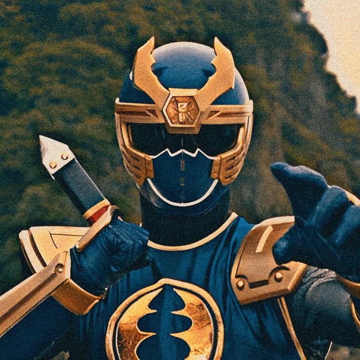 a man in a blue and gold costume holding two large knives while standing next to a mountain