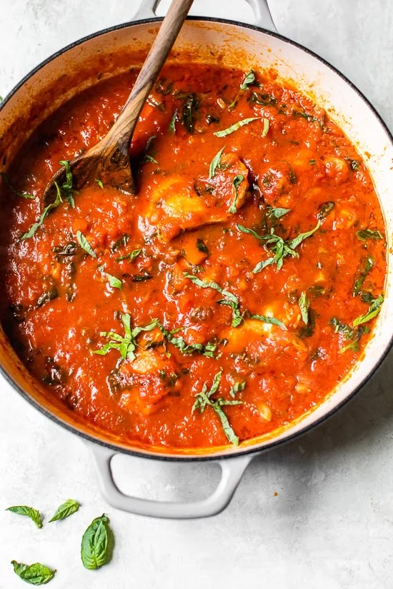 a pot filled with tomato sauce and garnished with fresh herbs on the side