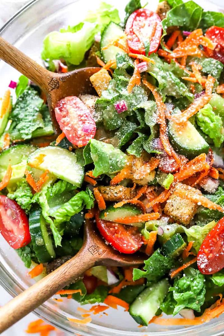 a salad in a glass bowl with wooden spoons