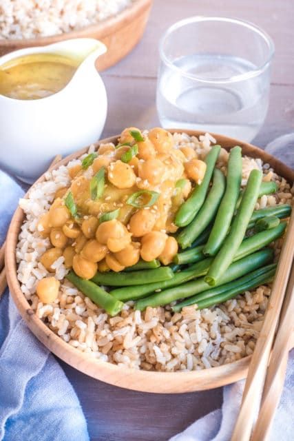 a wooden bowl filled with rice, beans and green beans next to some chopsticks